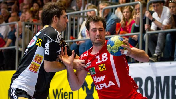 Ein Handballspieler im roten Trikot wird von einem Gegenspieler attackiert.