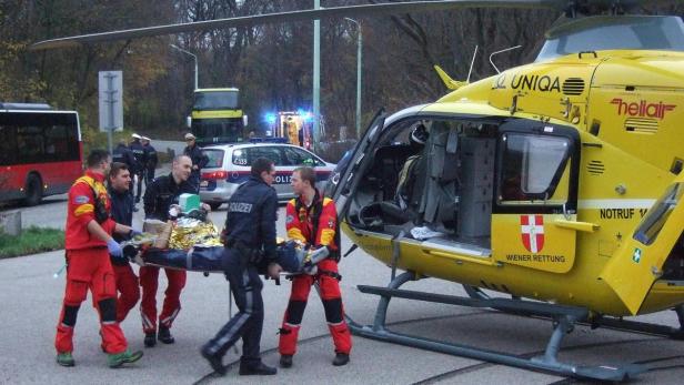 Rettungskräfte und Polizei transportieren eine Person auf einer Trage zu einem gelben Rettungshubschrauber.