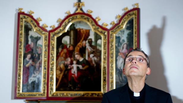 Ein Priester blickt auf ein Triptychon mit religiösen Motiven.