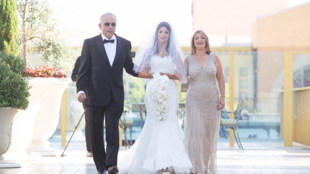Eine Braut wird von ihrem Vater und einer Frau zum Altar geführt.