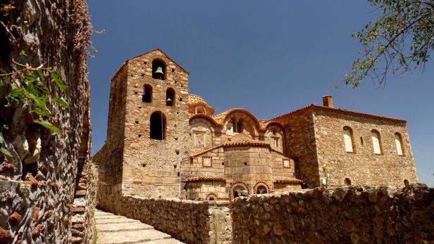 Eine mittelalterliche Kirche aus Stein mit einem Glockenturm unter blauem Himmel.