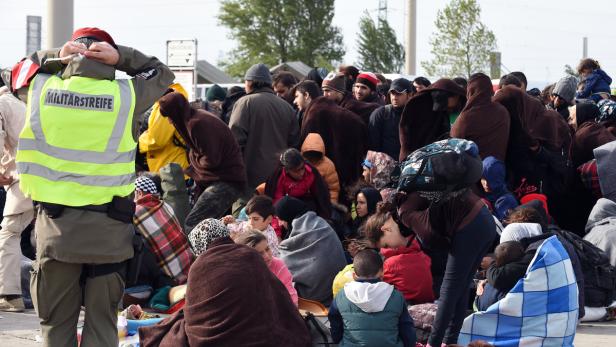 Eine Menschenmenge, viele in Decken gehüllt, wird von einem Soldaten bewacht.