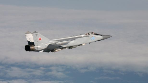 Ein graues MiG-25 Flugzeug fliegt vor einem bewölkten Himmel.