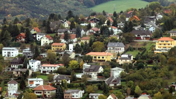 Blick auf eine Wohngegend mit Häusern unterschiedlicher Bauart an einem bewaldeten Hang.