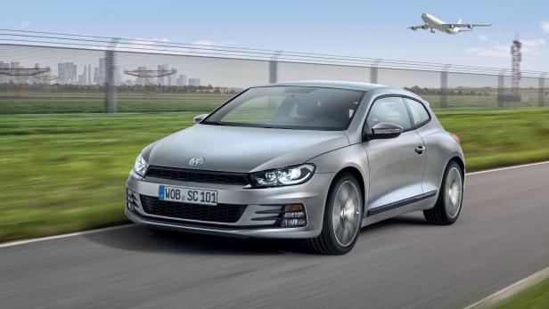 Ein silberner VW Scirocco fährt auf einer Straße entlang eines Flughafens.