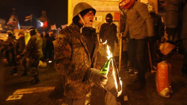 Ein Mann mit Helm hält einen Molotowcocktail in der Hand.