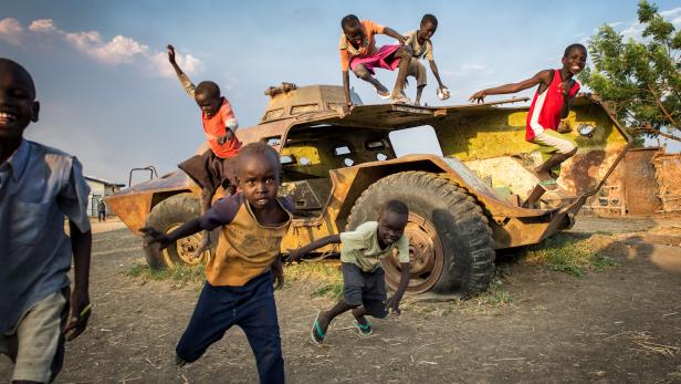 Eine Gruppe Kinder spielt auf und um ein verlassenes Militärfahrzeug.