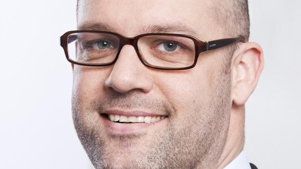 Ein lächelnder Mann mit Brille vor einem neutralen Hintergrund.