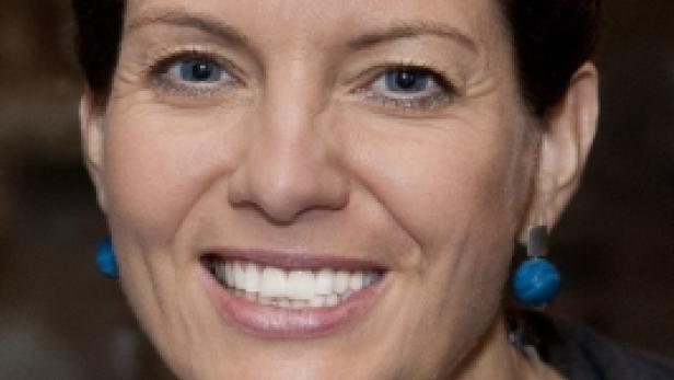 Eine lächelnde Frau mit kurzem braunem Haar und blauem Schmuck.
