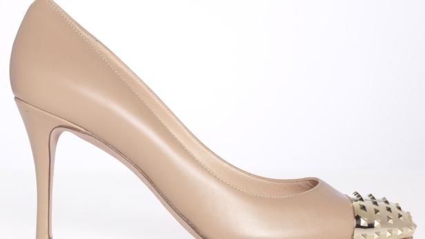 Ein beiger High Heel mit goldenen Nieten an der Spitze.