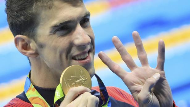Michael Phelps zeigt seine Goldmedaille und vier Finger.