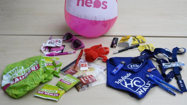 Ein Tisch mit Wahlkampfmaterialien verschiedener Parteien, darunter Neos, Grüne und FPÖ.