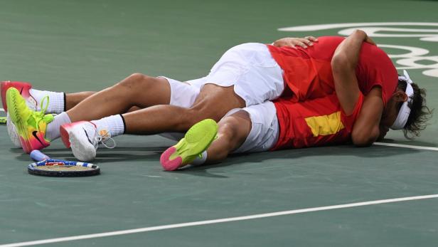 Zwei Tennisspieler liegen nach einem Match erschöpft auf dem Platz.