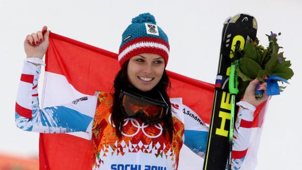 Eine österreichische Skirennläuferin feiert mit der österreichischen Flagge und einem Blumenstrauß.