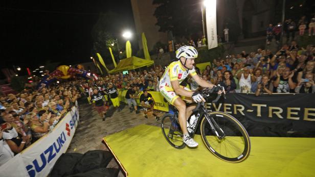 Ein Radfahrer fährt bei Nacht vor einer jubelnden Menschenmenge über eine Rampe.