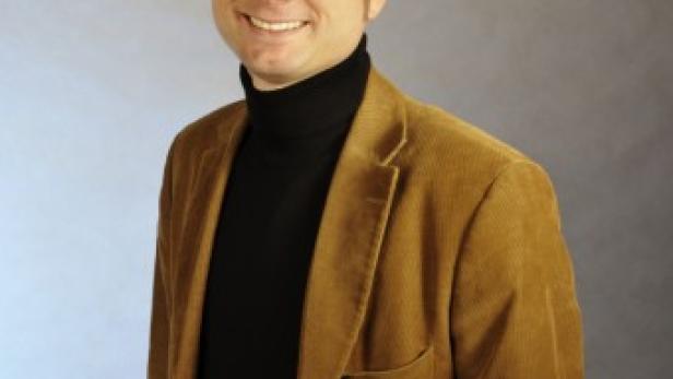 Ein Mann mit einem schwarzen Rollkragenpullover und einem Cordjackett lächelt in die Kamera.
