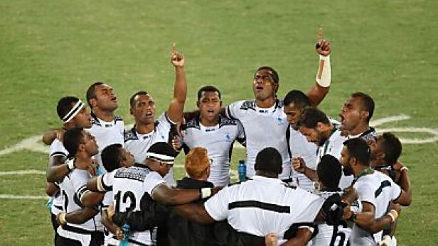 Fidschianische Rugbyspieler feiern gemeinsam mit erhobenen Armen einen Sieg.