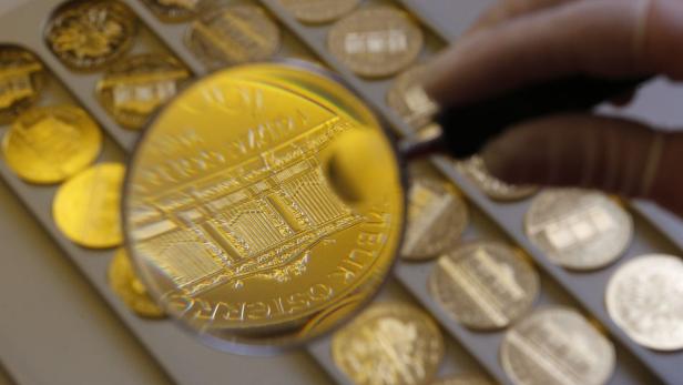 Eine Hand mit Handschuh untersucht eine Goldmünze der Republik Österreich mit einer Lupe.