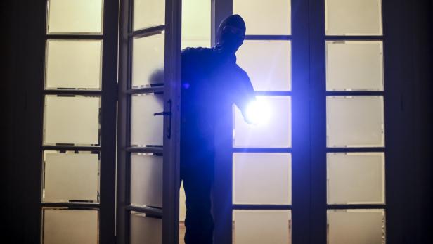 Einbrecher mit Taschenlampe kommt in der Dunkelheit durch eine Tür