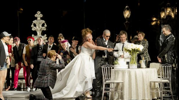 Eine Hochzeitsgesellschaft schneidet gemeinsam eine Hochzeitstorte an.