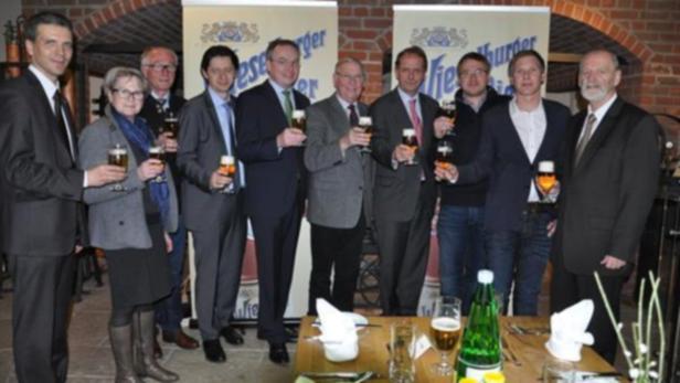 Eine Gruppe von Personen steht mit Biergläsern vor einem Banner der Brauerei Kieselberger.