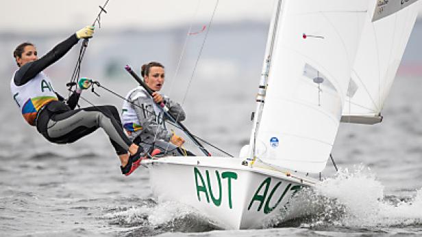 Zwei Seglerinnen steuern ein Segelboot mit der Aufschrift „AUT“ auf dem Wasser.