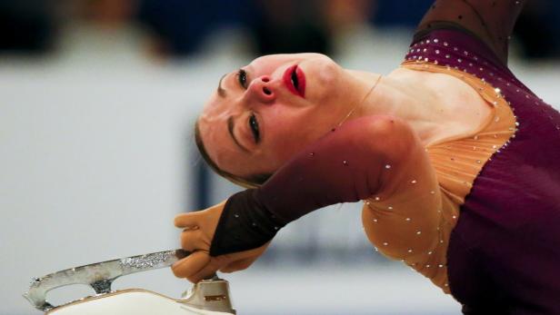 Eine Eiskunstläuferin in einem burgunderfarbenen Kleid führt eine Drehung auf dem Eis aus.