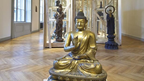 Eine goldene Buddha-Statue sitzt in einem Raum mit weiteren Statuen in Vitrinen.