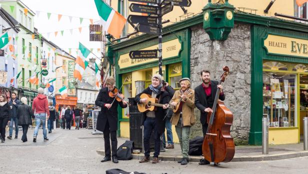 Eine Straßenmusikgruppe spielt in einer mit irischen Flaggen geschmückten Straße in Galway, Irland.