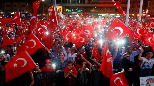 Eine Menschenmenge schwenkt türkische Flaggen bei einer abendlichen Veranstaltung.