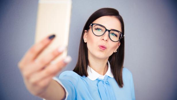 Eine Frau mit Brille macht ein Selfie mit ihrem Smartphone.