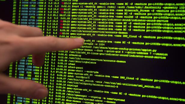 Ein Finger zeigt auf einen Computermonitor mit grünem Code.