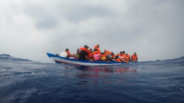Migrants on a wooden boat wait for the Italian Guardia Costiera in the Mediterranean Sea