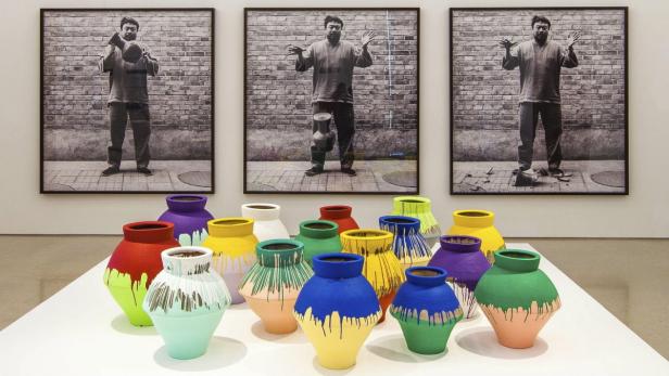 Eine Ausstellung mit farbig bemalten Vasen vor drei Schwarzweißfotografien von Ai Weiwei.