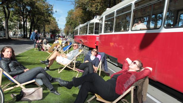 Menschen entspannen in Liegestühlen neben einer roten Straßenbahn.