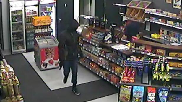 Eine vermummte Person steht in einem Geschäft vor Regalen mit Waren.