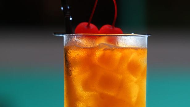 Ein Longdrink mit Eis und Kirschen wird mit einem Strohhalm serviert.