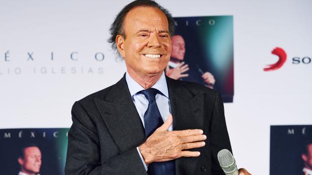 Julio Iglesias lächelt bei einer Veranstaltung und hält ein Mikrofon.