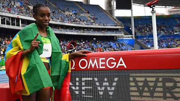 Eine Athletin mit der Flagge von Ruanda posiert vor einer Anzeigetafel im Stadion.