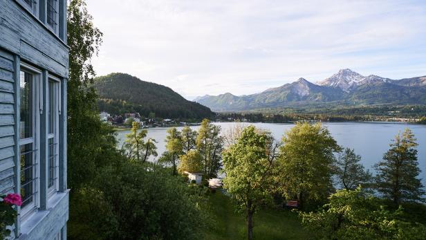 Blick auf einen See und schneebedeckte Berge von einem hölzernen Gebäude aus.
