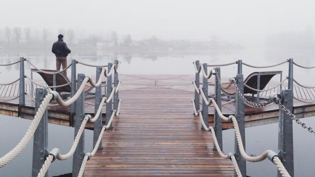 Ein Mann steht am Ende eines Holzstegs im Nebel.