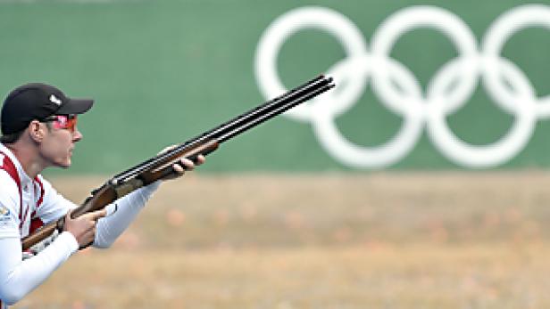 Ein Schütze zielt mit einem Gewehr vor dem Hintergrund der Olympischen Ringe.