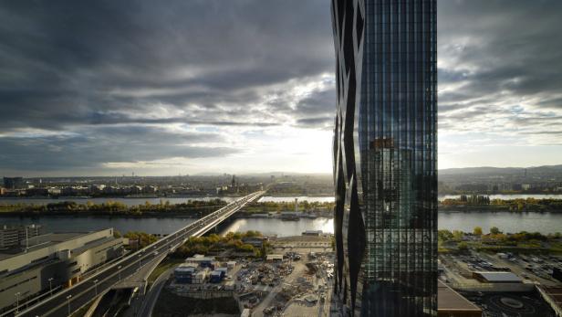 Blick auf Wien mit der Donau, einer Brücke und einem modernen Hochhaus im Vordergrund.