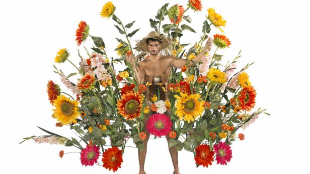 Ein Mann mit Strohhut und Blumen geschmückt vor einem weißen Hintergrund.