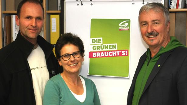 Drei Personen posieren vor einem Plakat der Grünen Partei.