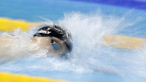 Ein Schwimmer mit Badekappe und Schwimmbrille taucht ins Wasser.