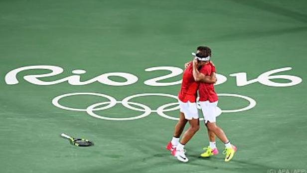 Zwei Tennisspieler umarmen sich vor dem Logo der Olympischen Spiele in Rio 2016.