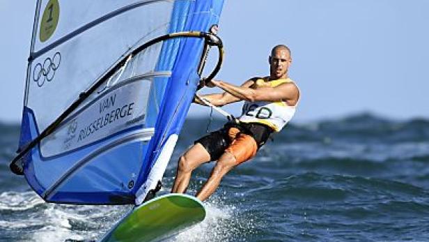 Ein Windsurfer auf dem Wasser mit blauem Himmel im Hintergrund.