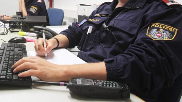 Ein Polizist sitzt an einem Schreibtisch und tippt auf einer Tastatur, während er etwas aufschreibt.