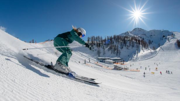 Eine Skifahrerin fährt an einem sonnigen Tag eine Skipiste hinunter.